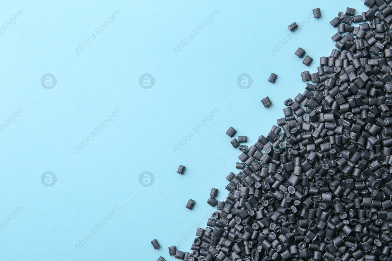 Photo of Pile of black plastic granules on light blue background, top view. Space for text