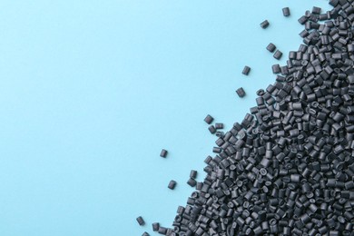 Photo of Pile of black plastic granules on light blue background, top view. Space for text