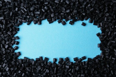 Photo of Frame of black plastic granules on light blue background, top view. Space for text