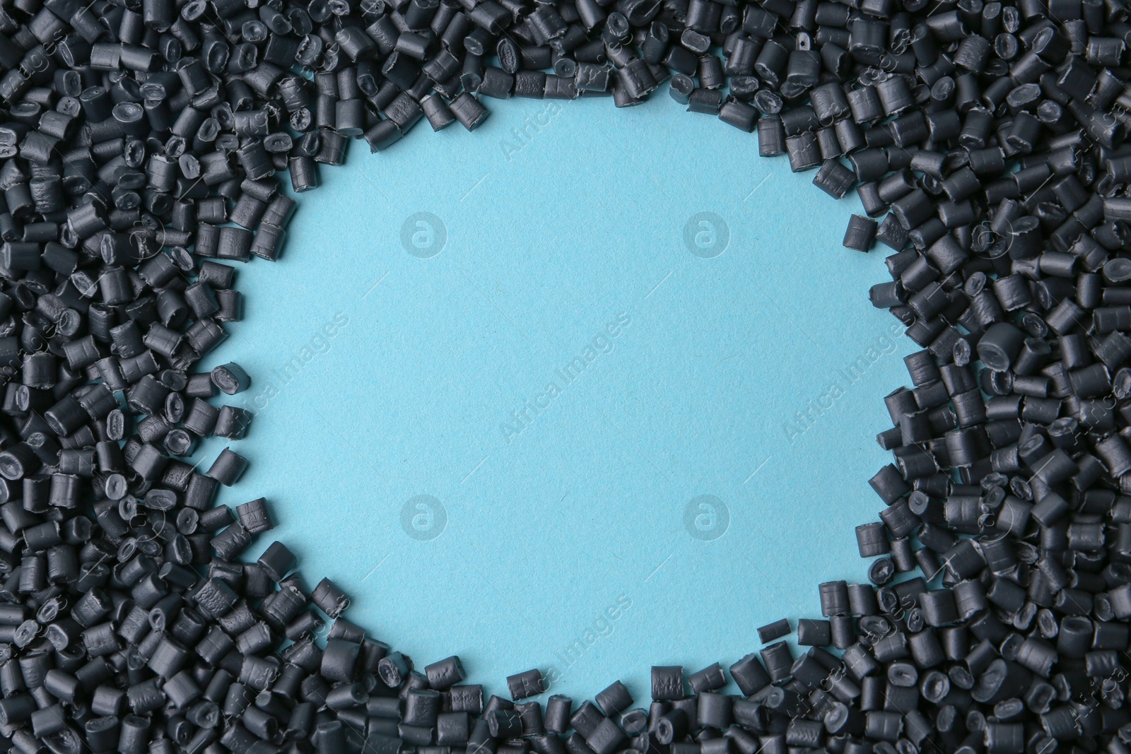 Photo of Frame of black plastic granules on light blue background, top view. Space for text