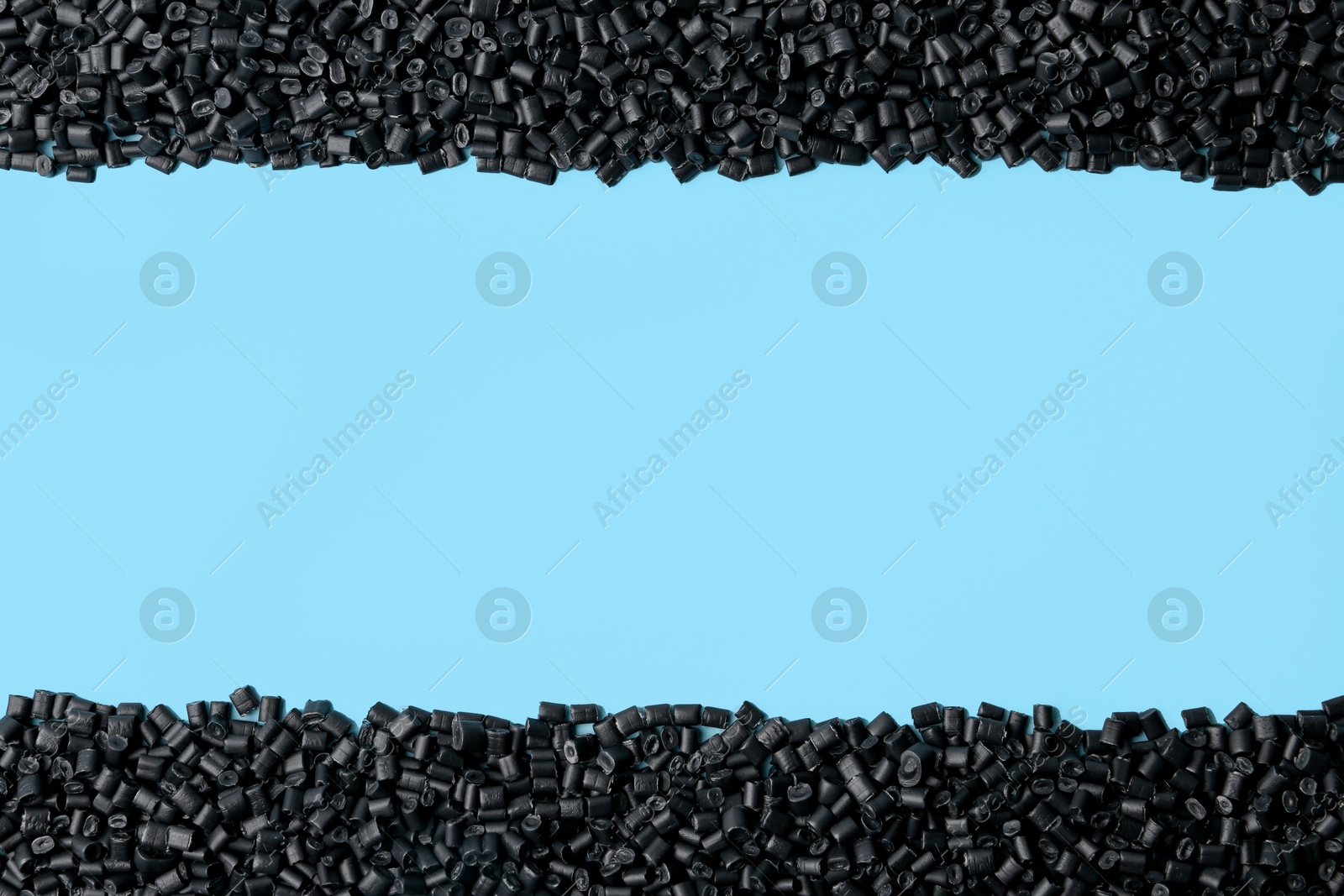 Photo of Pile of black plastic granules on light blue background, top view. Space for text