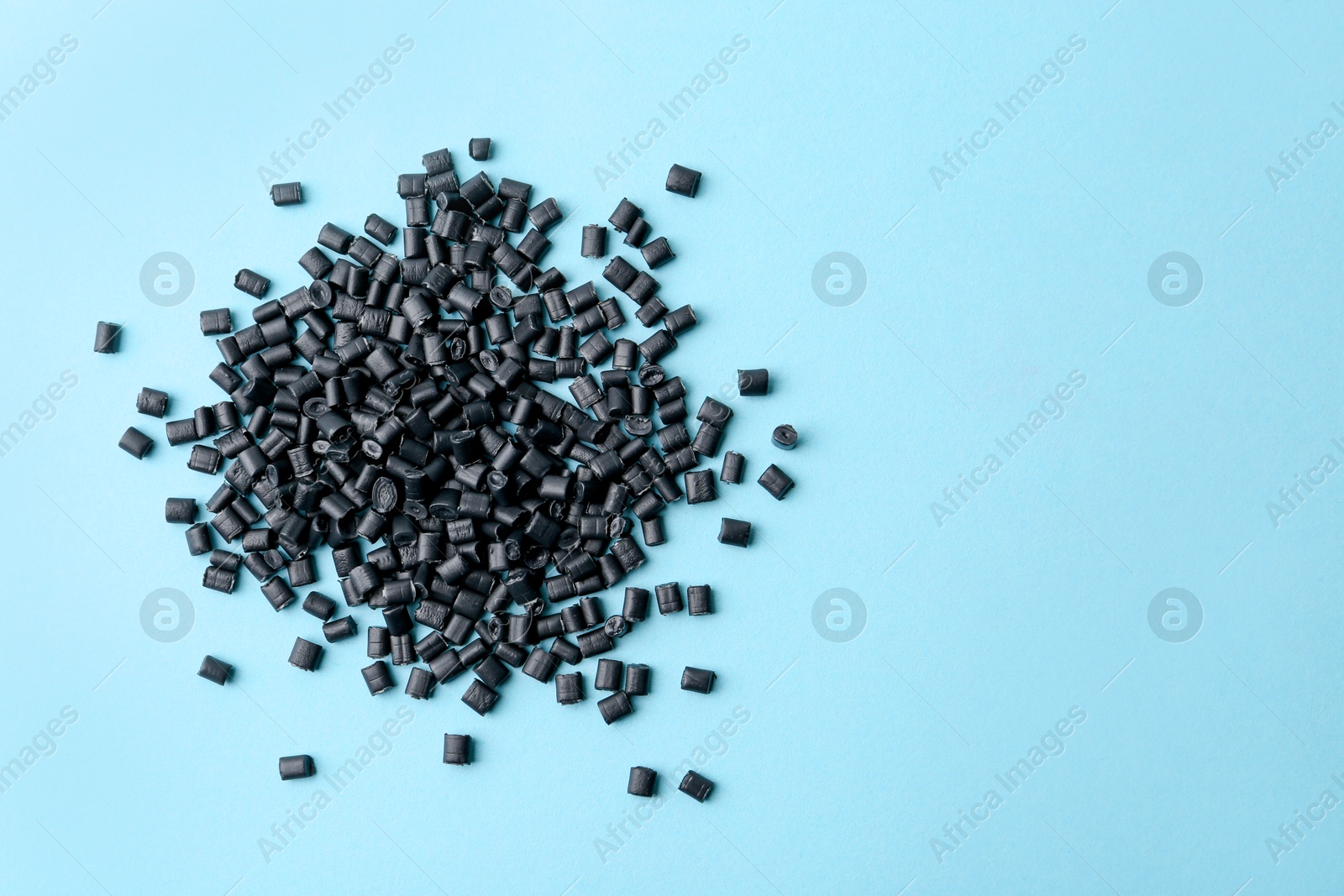 Photo of Pile of black plastic granules on light blue background, top view. Space for text