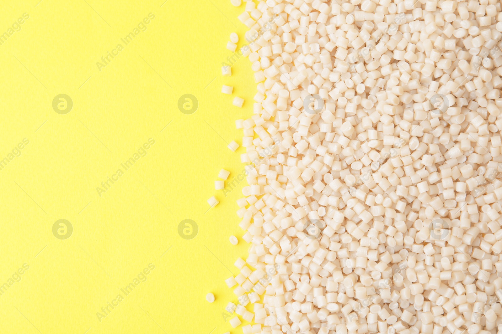 Photo of Pile of plastic granules on yellow background, top view. Space for text