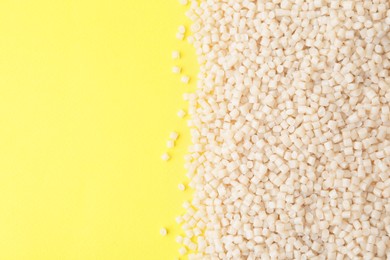 Photo of Pile of plastic granules on yellow background, top view. Space for text