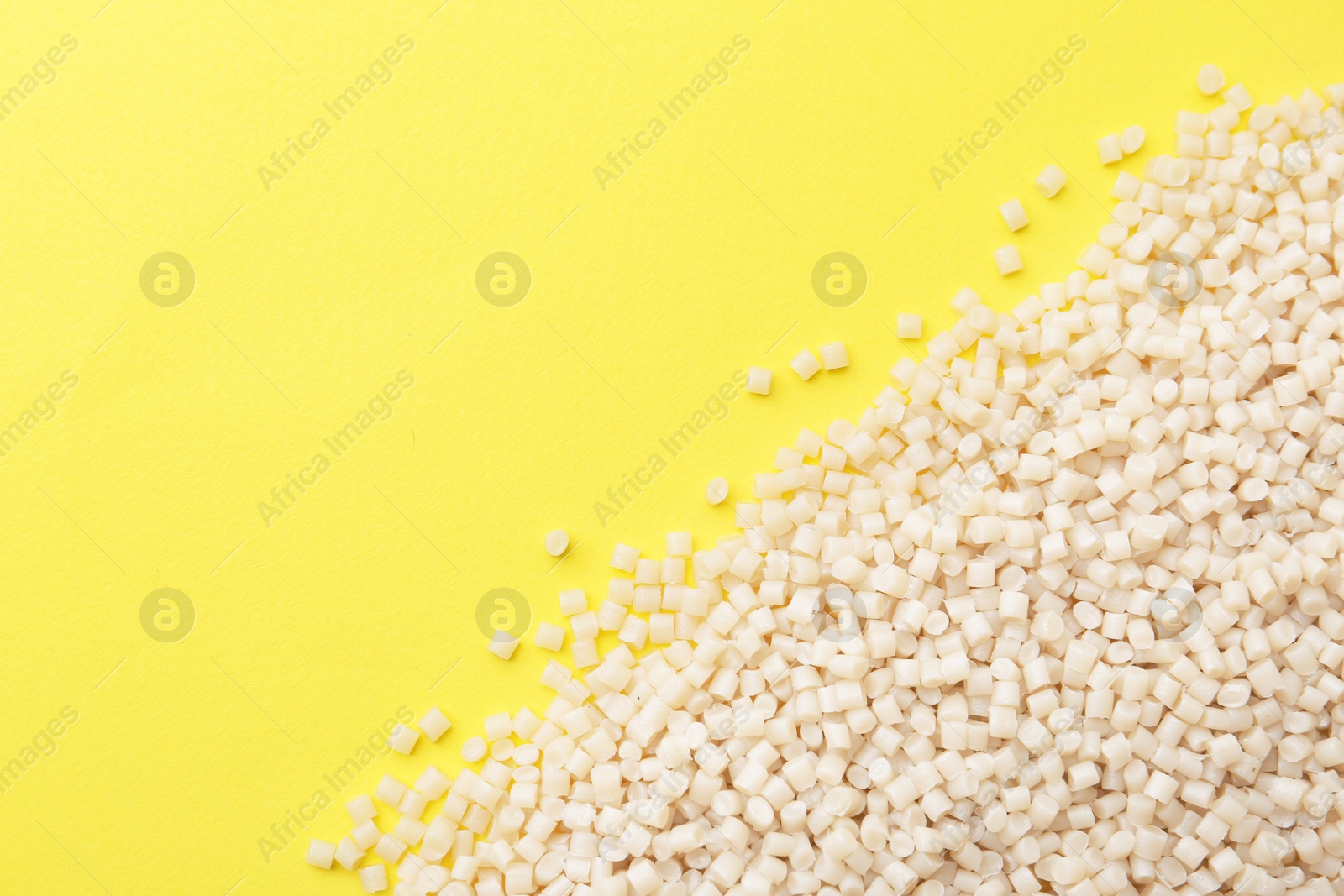 Photo of Pile of plastic granules on yellow background, top view. Space for text