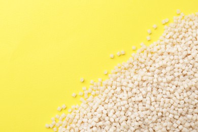 Photo of Pile of plastic granules on yellow background, top view. Space for text