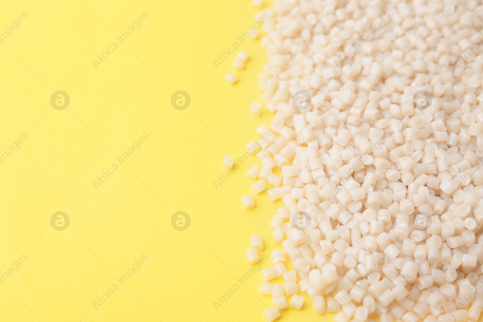 Photo of Pile of plastic granules on yellow background, closeup. Space for text