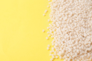 Photo of Pile of plastic granules on yellow background, closeup. Space for text