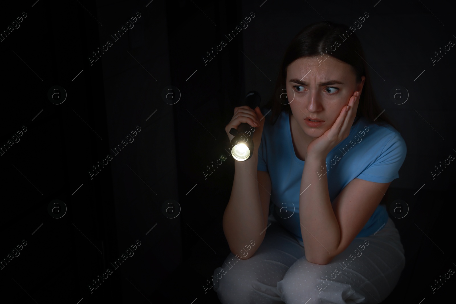 Photo of Fear of darkness. Scared young woman with flashlight indoors at night, space for text