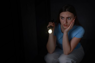 Photo of Fear of darkness. Scared young woman with flashlight indoors at night, space for text