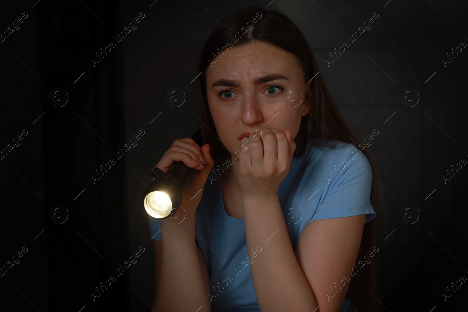 Photo of Fear of darkness. Scared young woman with flashlight indoors at night