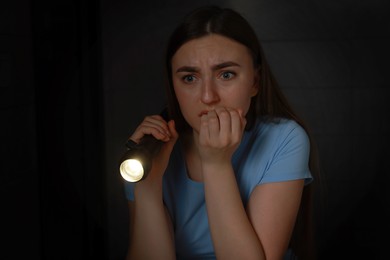 Photo of Fear of darkness. Scared young woman with flashlight indoors at night