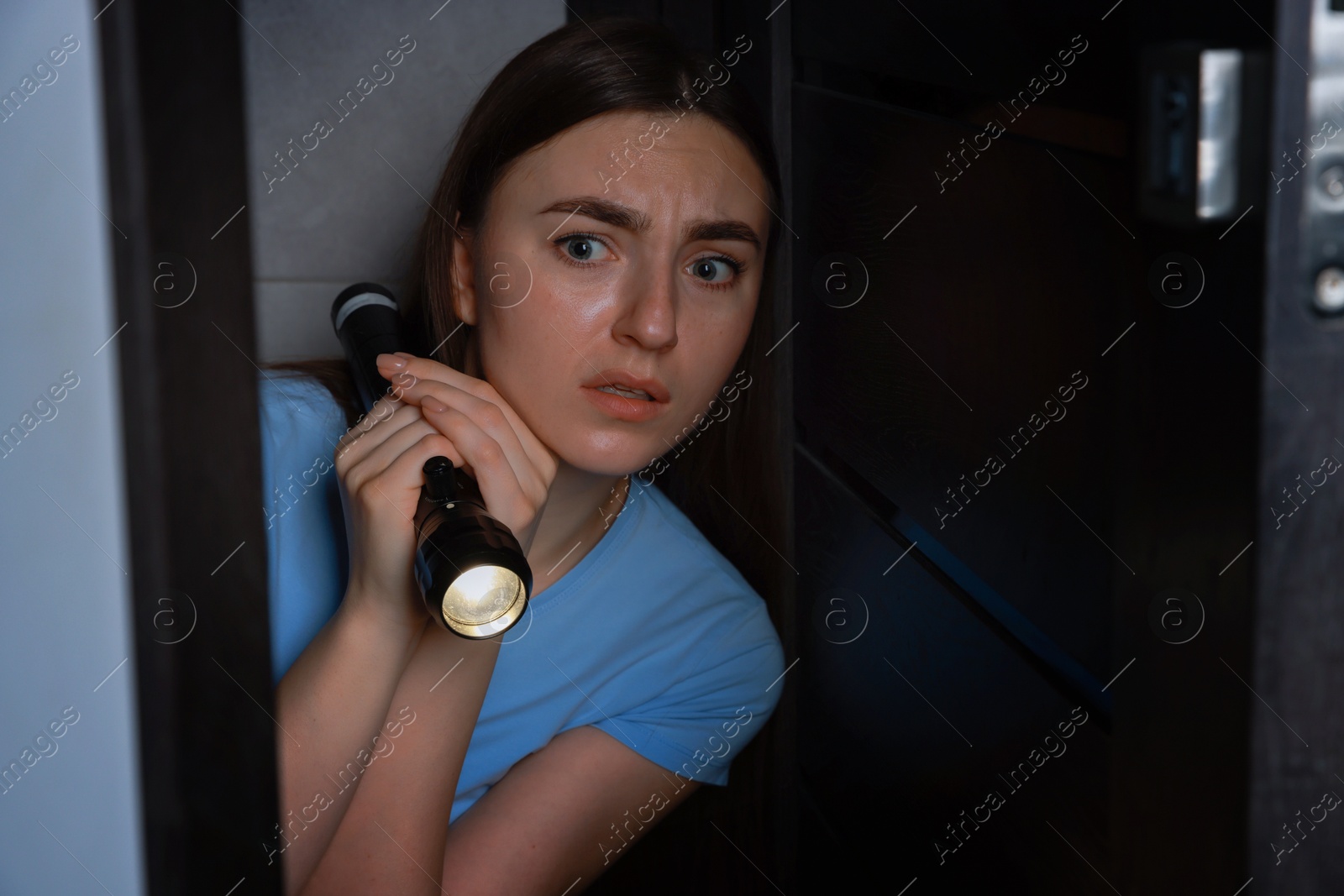 Photo of Fear of darkness. Scared young woman with flashlight indoors at night, space for text