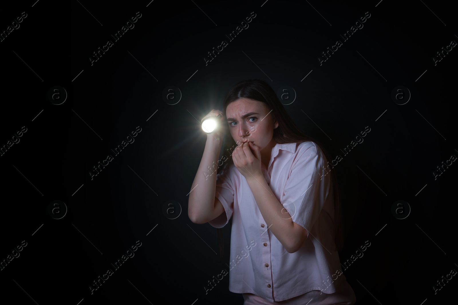 Photo of Fear of darkness. Scared young woman with flashlight on black background