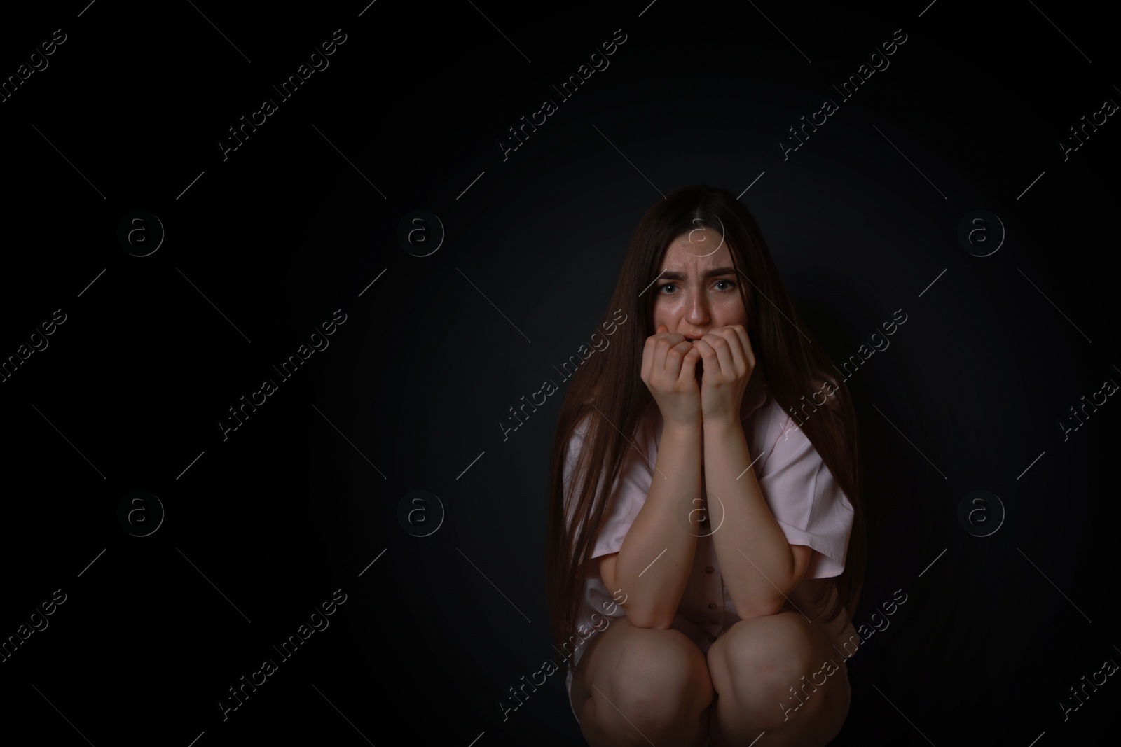 Photo of Fear of darkness. Scared young woman on black background, space for text