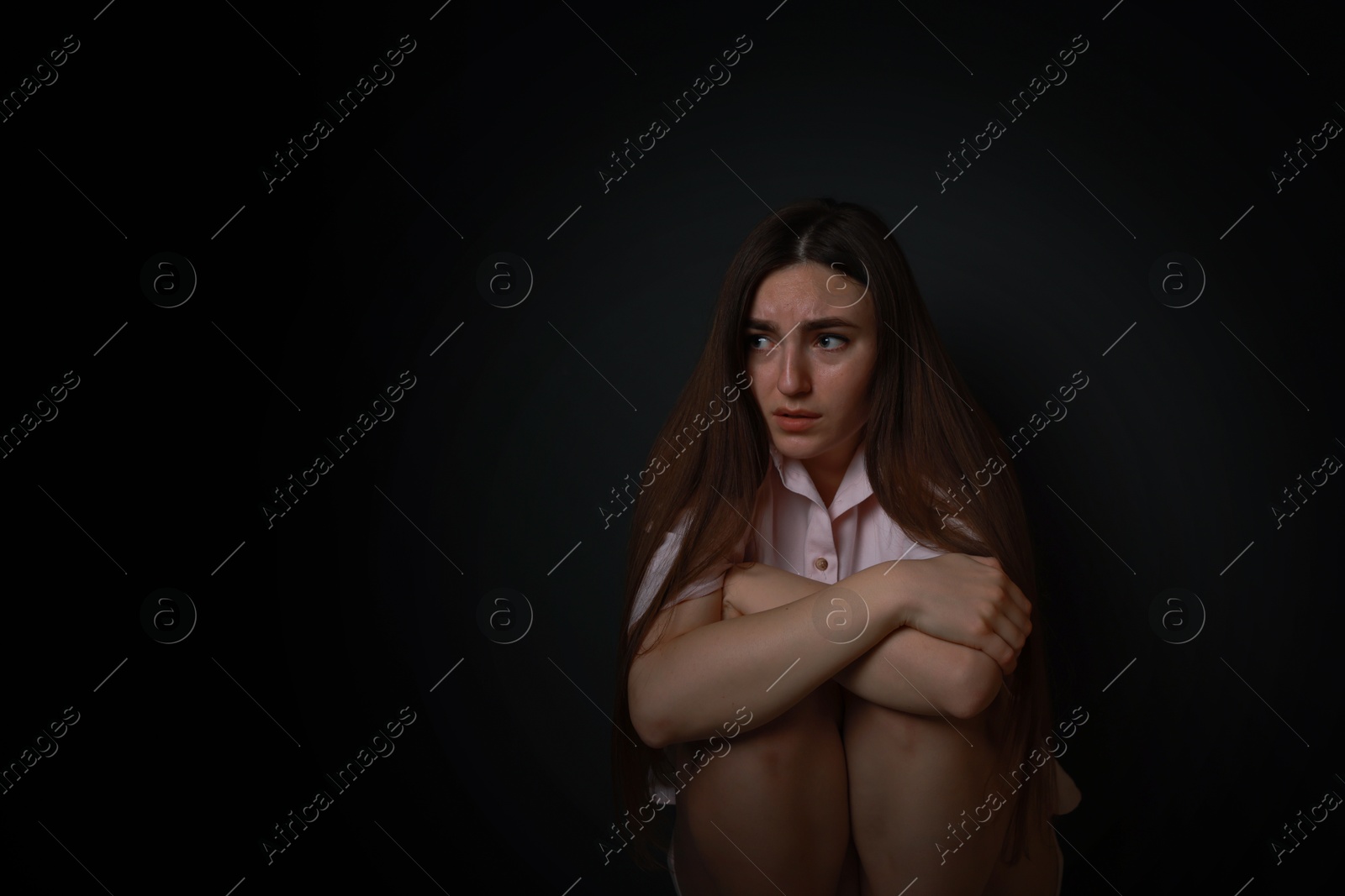 Photo of Fear of darkness. Scared young woman on black background, space for text