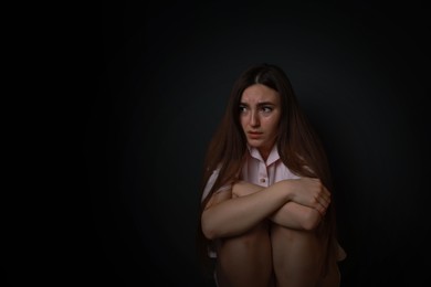 Photo of Fear of darkness. Scared young woman on black background, space for text