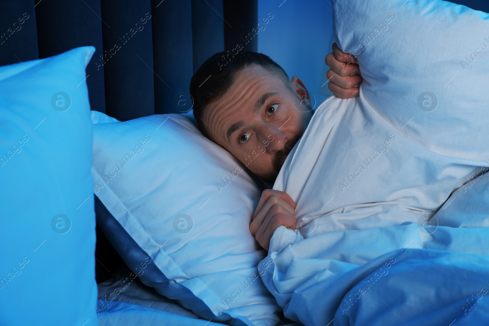 Photo of Fear of darkness. Scared man lying on bed in room at night