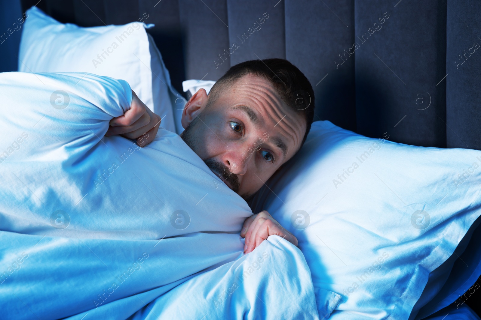 Photo of Fear of darkness. Scared man lying on bed in room at night