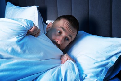 Photo of Fear of darkness. Scared man lying on bed in room at night