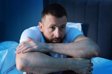 Photo of Fear of darkness. Scared man sitting on bed in room at night