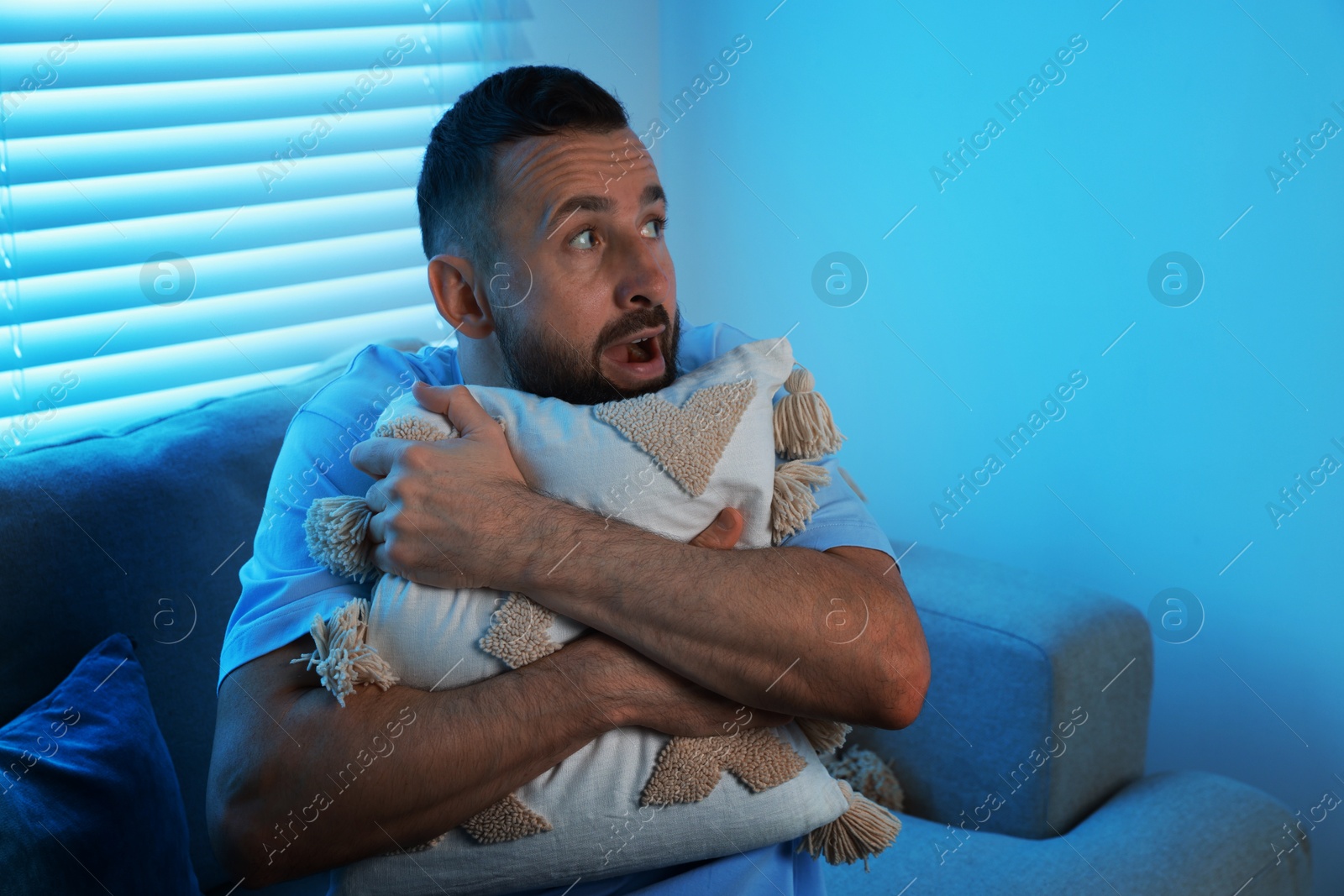 Photo of Fear of darkness. Scared man hugging pillow on couch in dark room, space for text