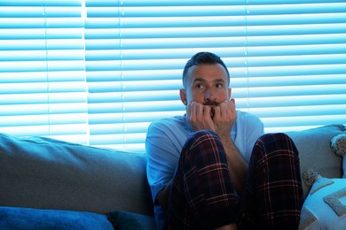 Photo of Fear of darkness. Scared man on couch in dark room, space for text