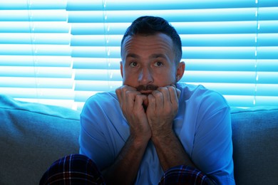 Photo of Fear of darkness. Scared man on couch in dark room