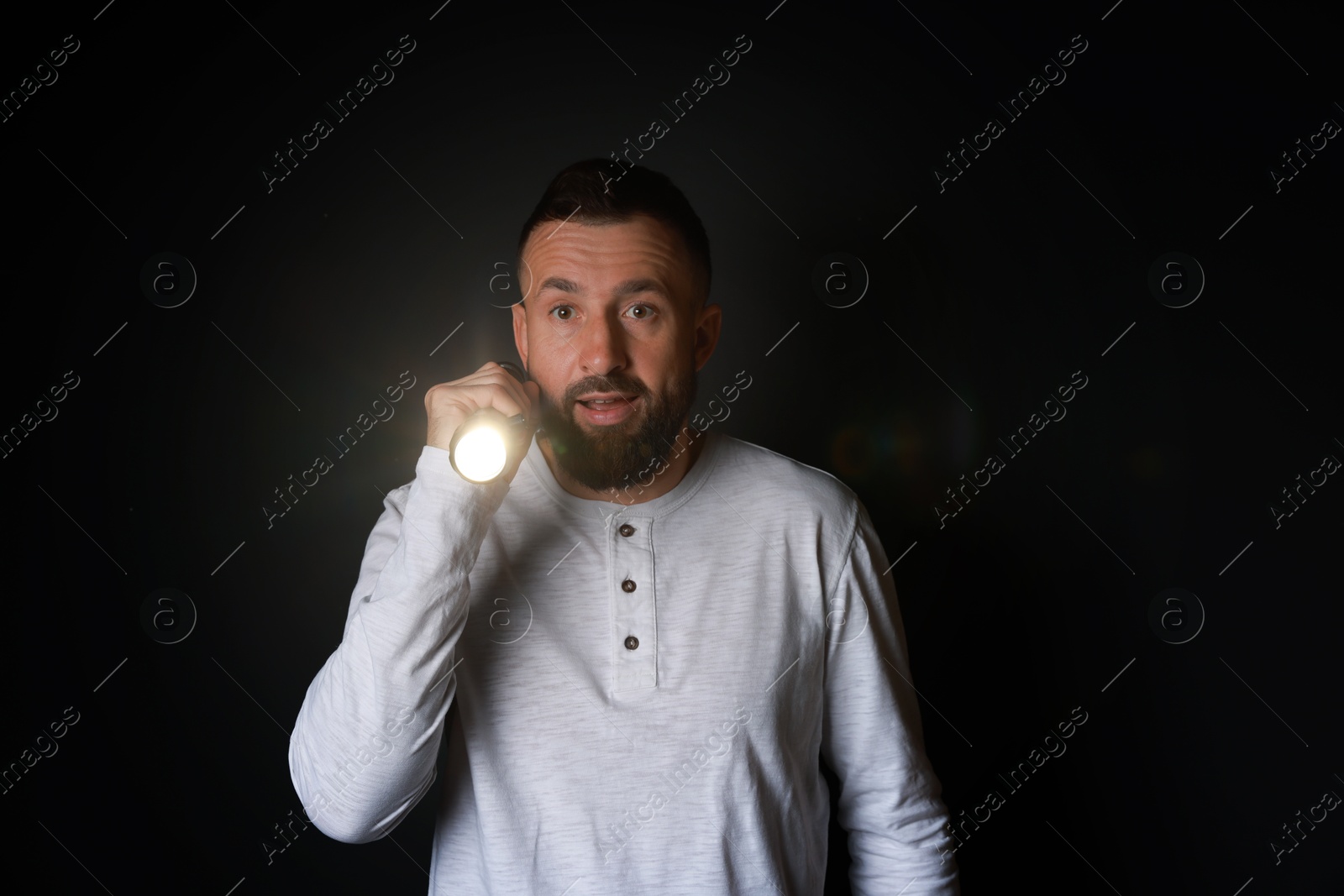 Photo of Fear of darkness. Scared man with flashlight on black background