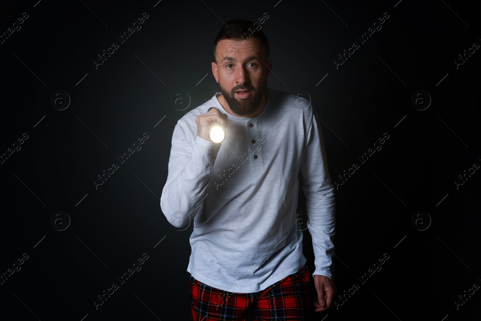 Photo of Fear of darkness. Scared man with flashlight on black background