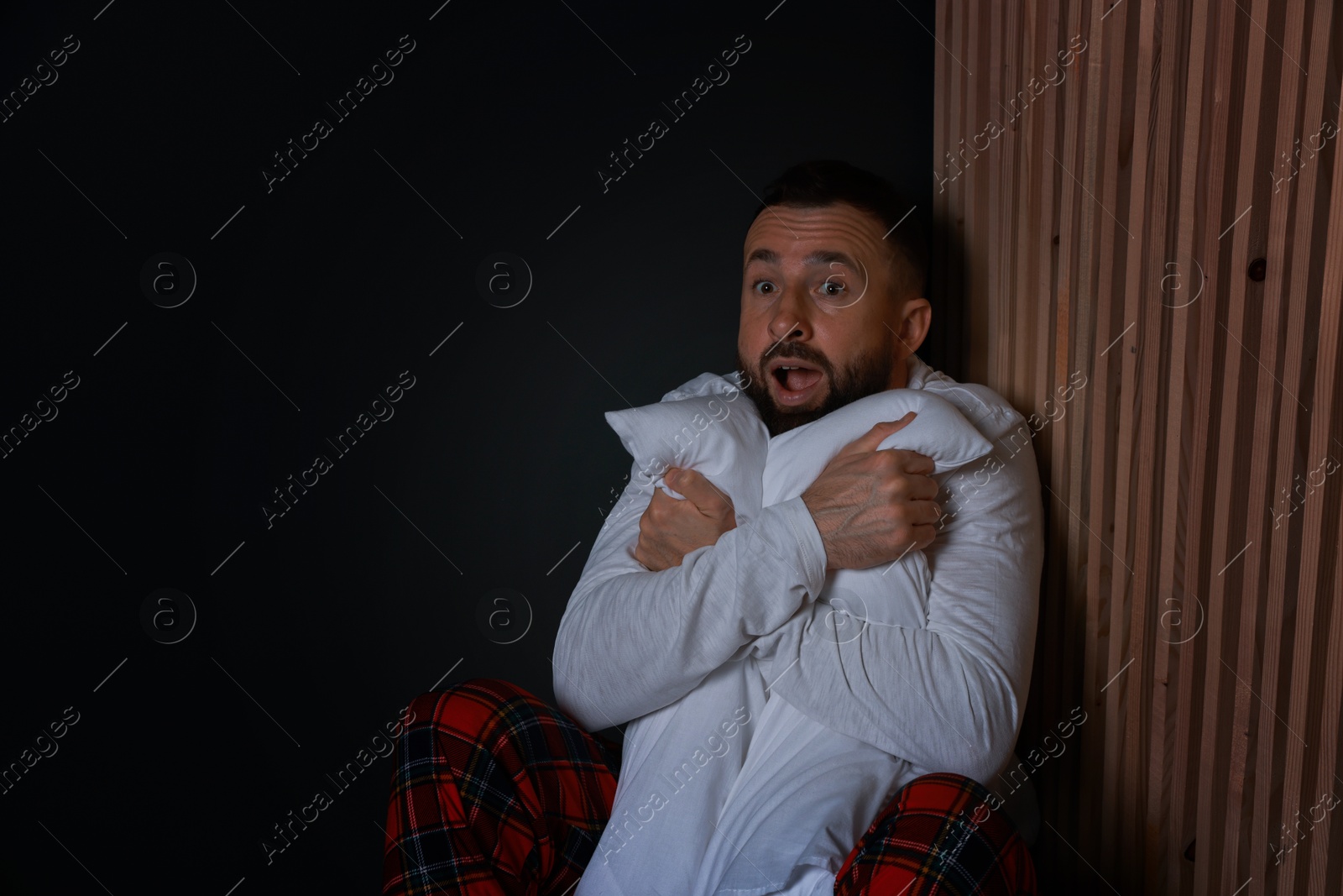 Photo of Fear of darkness. Scared man hugging pillow indoors at night