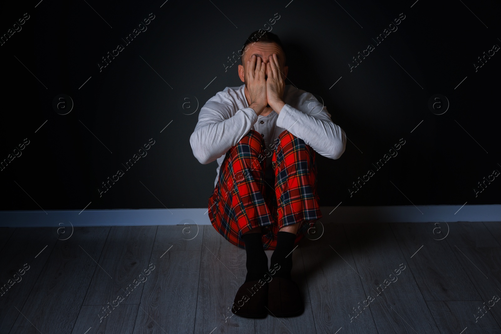 Photo of Fear of darkness. Scared man hiding his face indoors at night