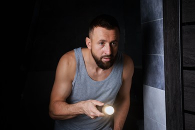 Photo of Fear of darkness. Scared man with flashlight in room at night