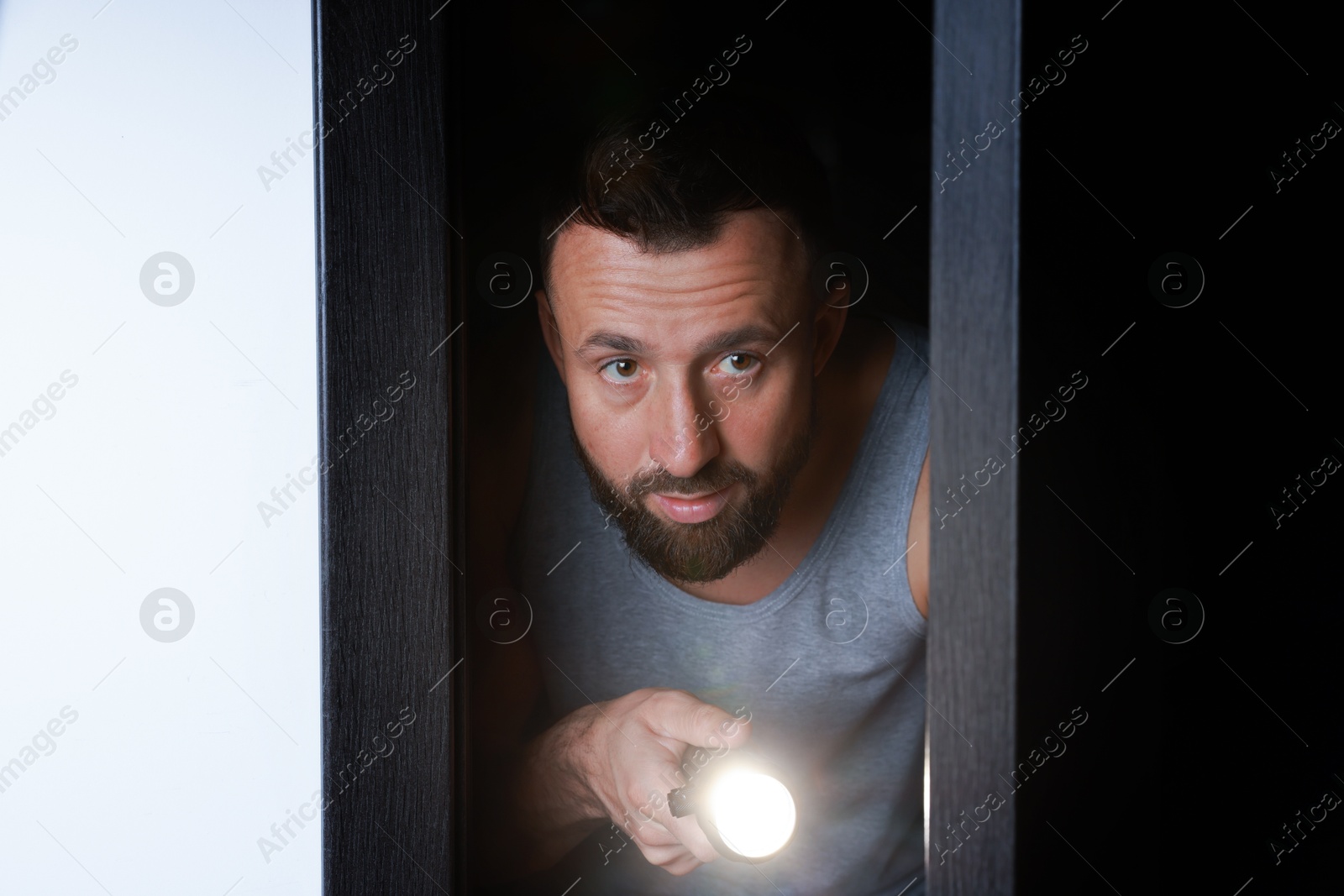 Photo of Fear of darkness. Scared man with flashlight in room at night