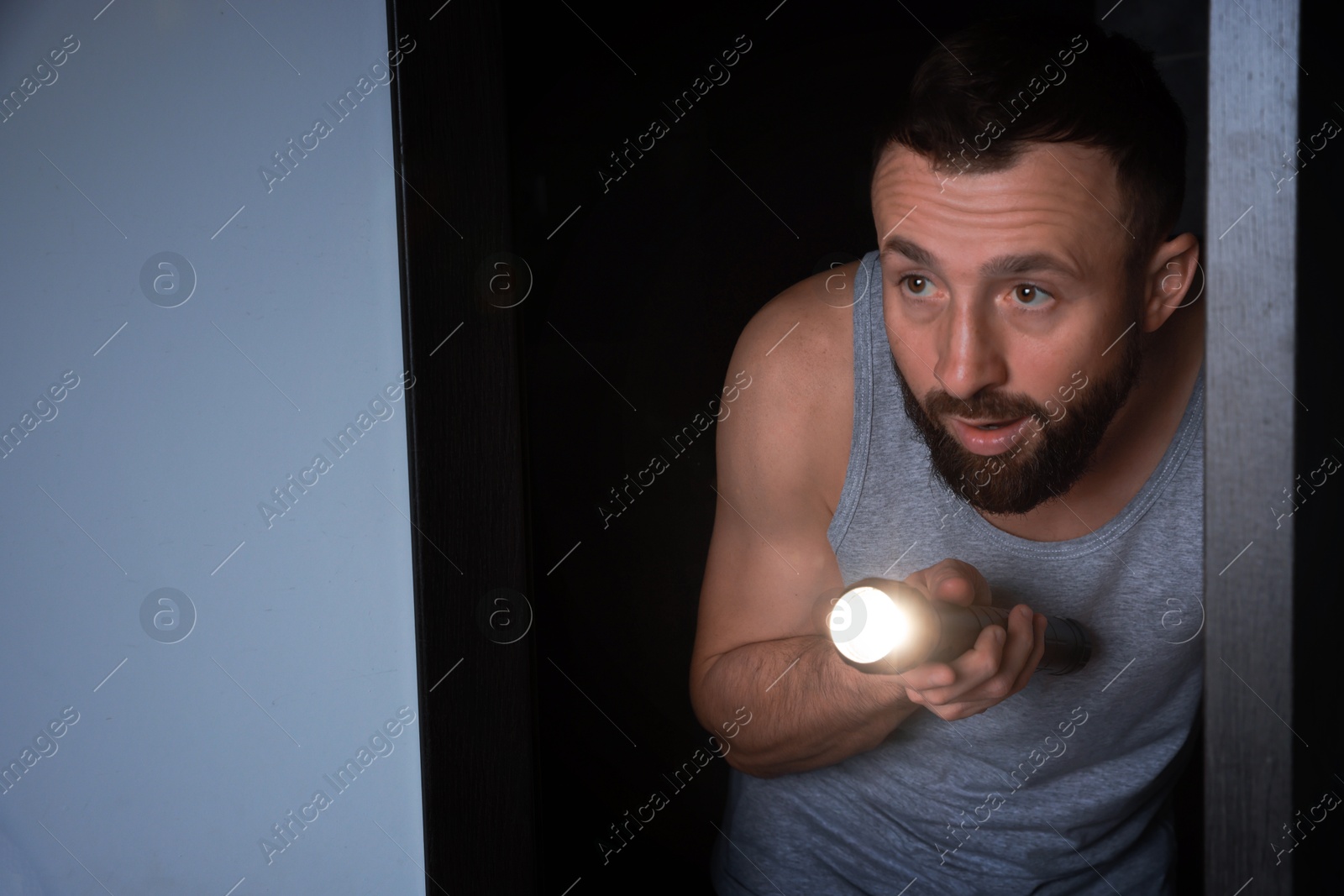 Photo of Fear of darkness. Scared man with flashlight in room at night, space for text