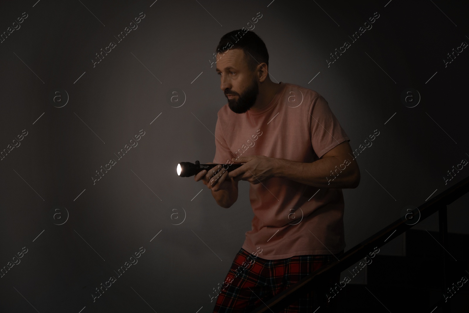 Photo of Fear of darkness. Scared man with flashlight indoors at night, space for text