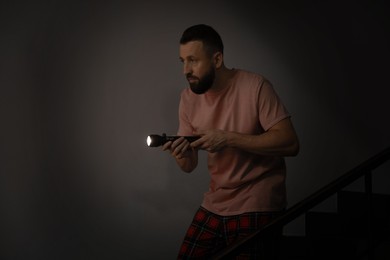 Photo of Fear of darkness. Scared man with flashlight indoors at night, space for text