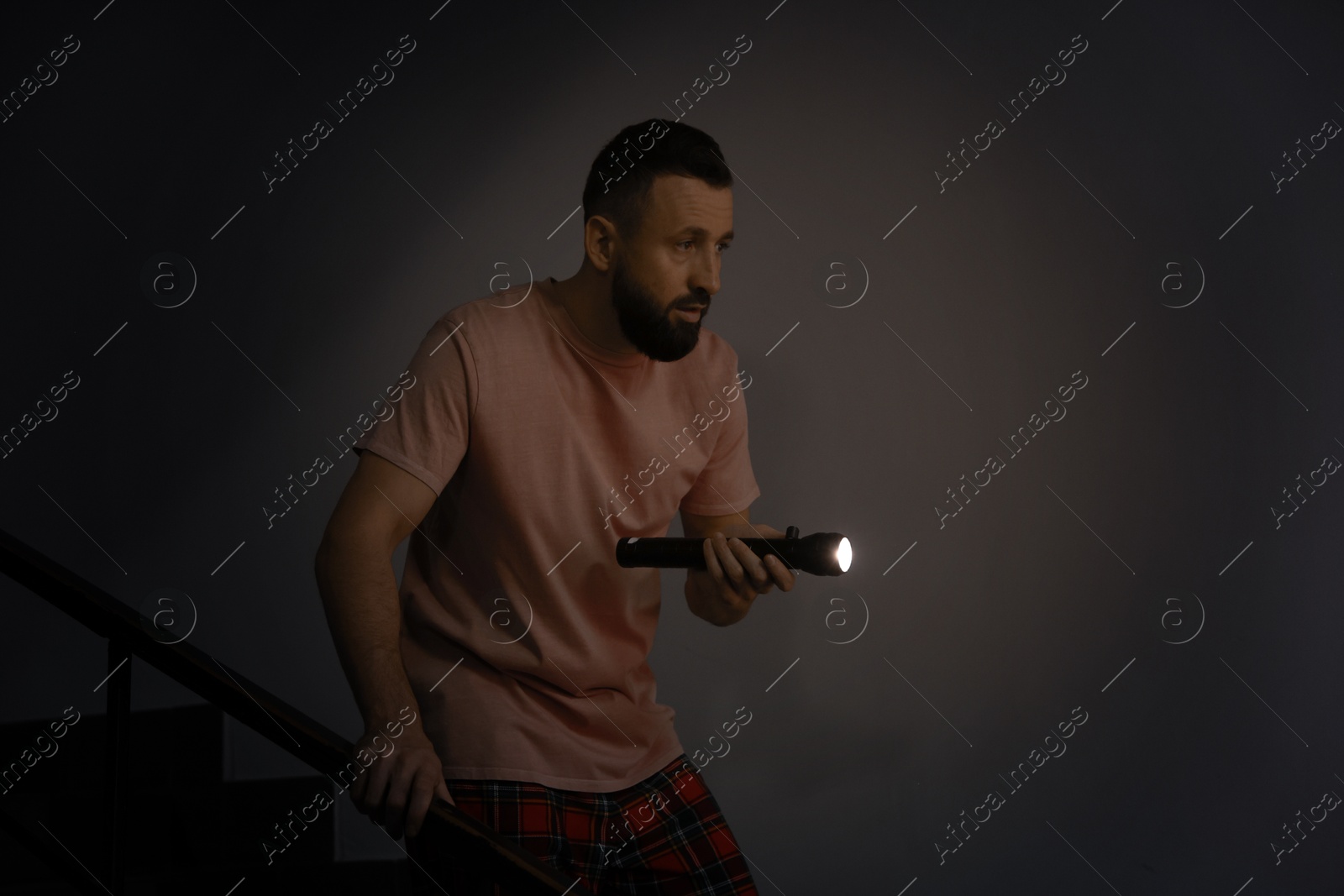 Photo of Fear of darkness. Scared man with flashlight indoors at night, space for text