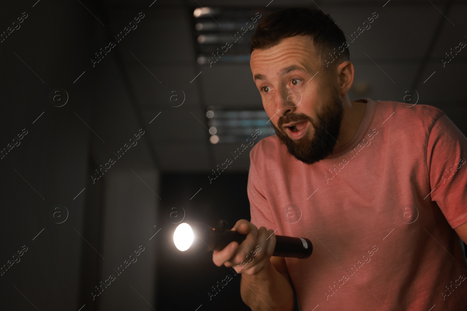 Photo of Fear of darkness. Scared man with flashlight indoors at night, space for text