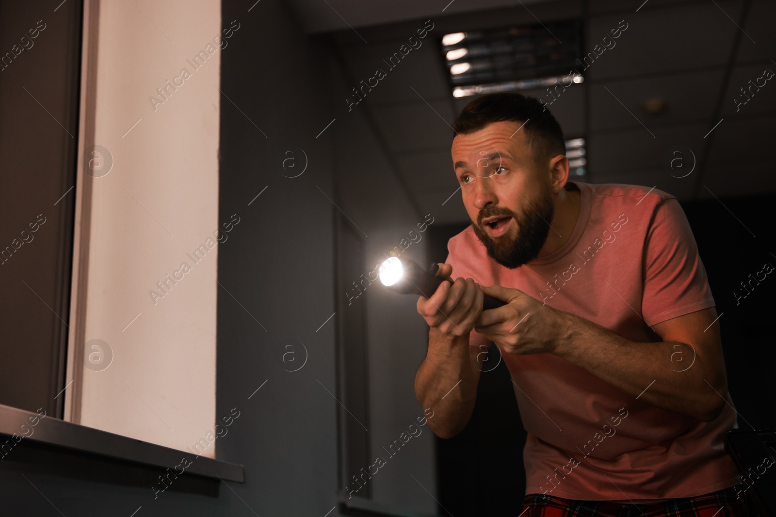 Photo of Fear of darkness. Scared man with flashlight indoors at night