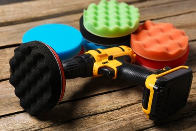 Photo of Electric screwdriver with different polish pads on wooden background, closeup