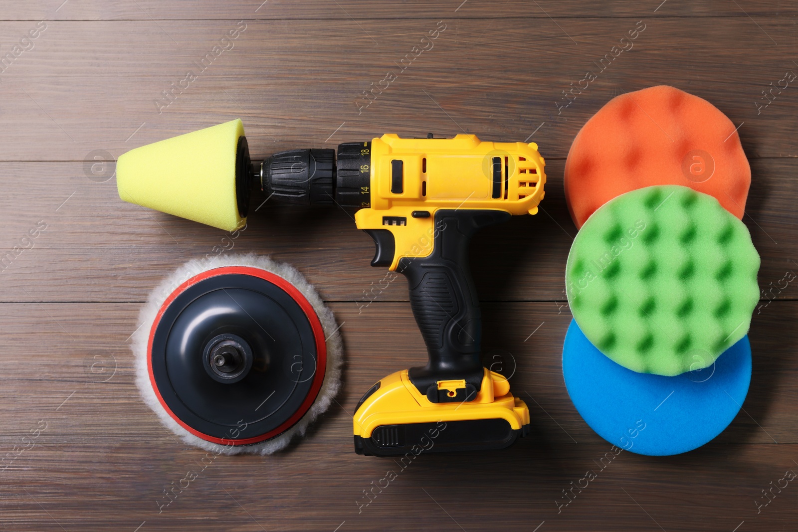 Photo of Electric screwdriver with different polish pads on wooden background, flat lay