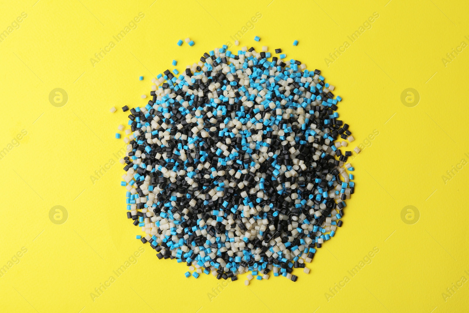 Photo of Pile of colorful plastic granules on yellow background, top view