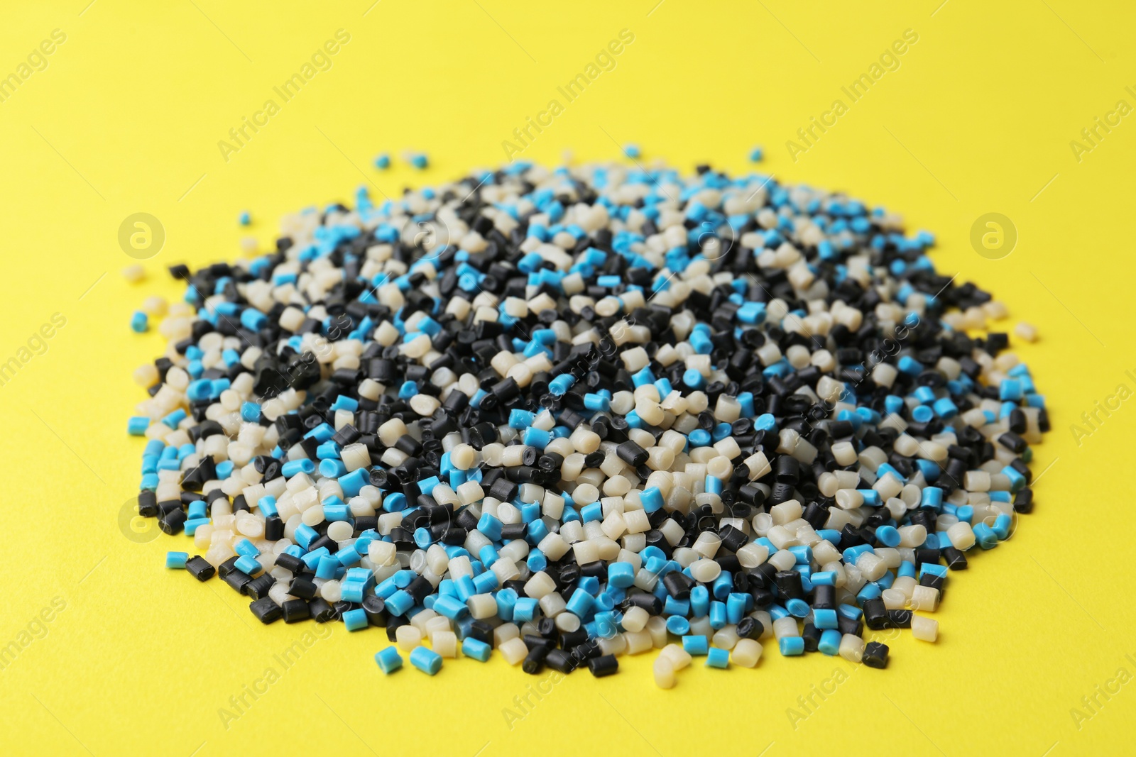 Photo of Pile of colorful plastic granules on yellow background, closeup