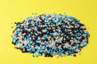 Photo of Pile of colorful plastic granules on yellow background, closeup