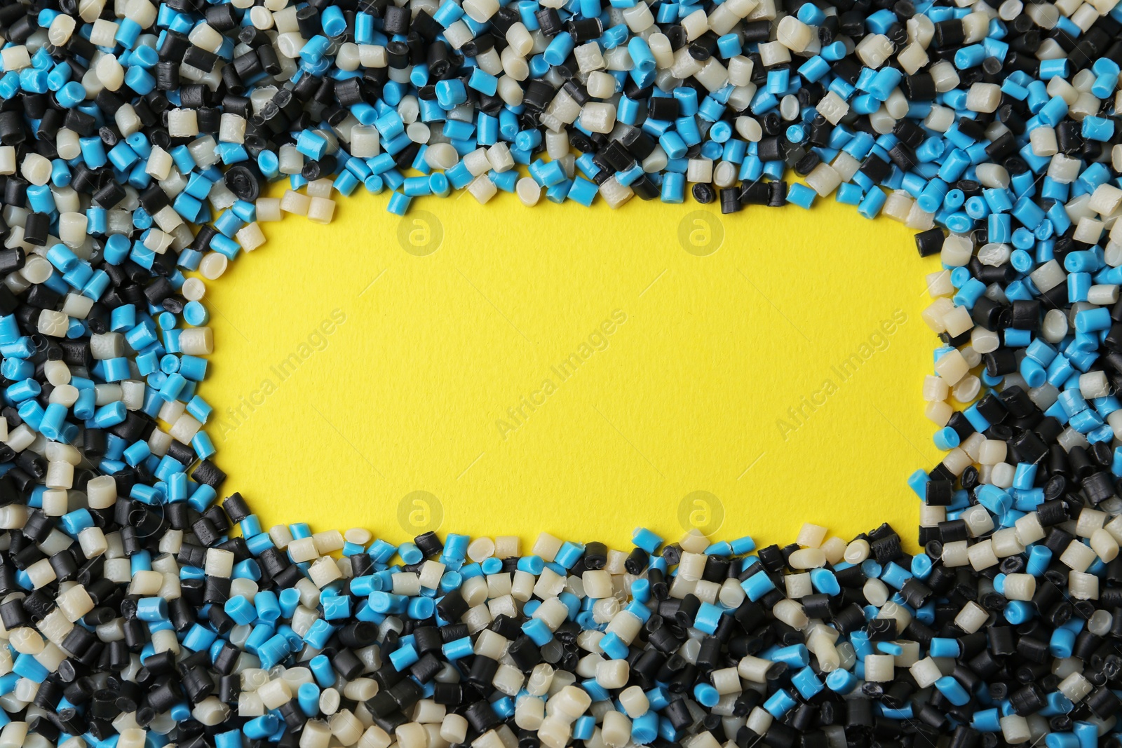 Photo of Frame of colorful plastic granules on yellow background, top view. Space for text