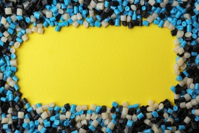 Photo of Frame of colorful plastic granules on yellow background, top view. Space for text