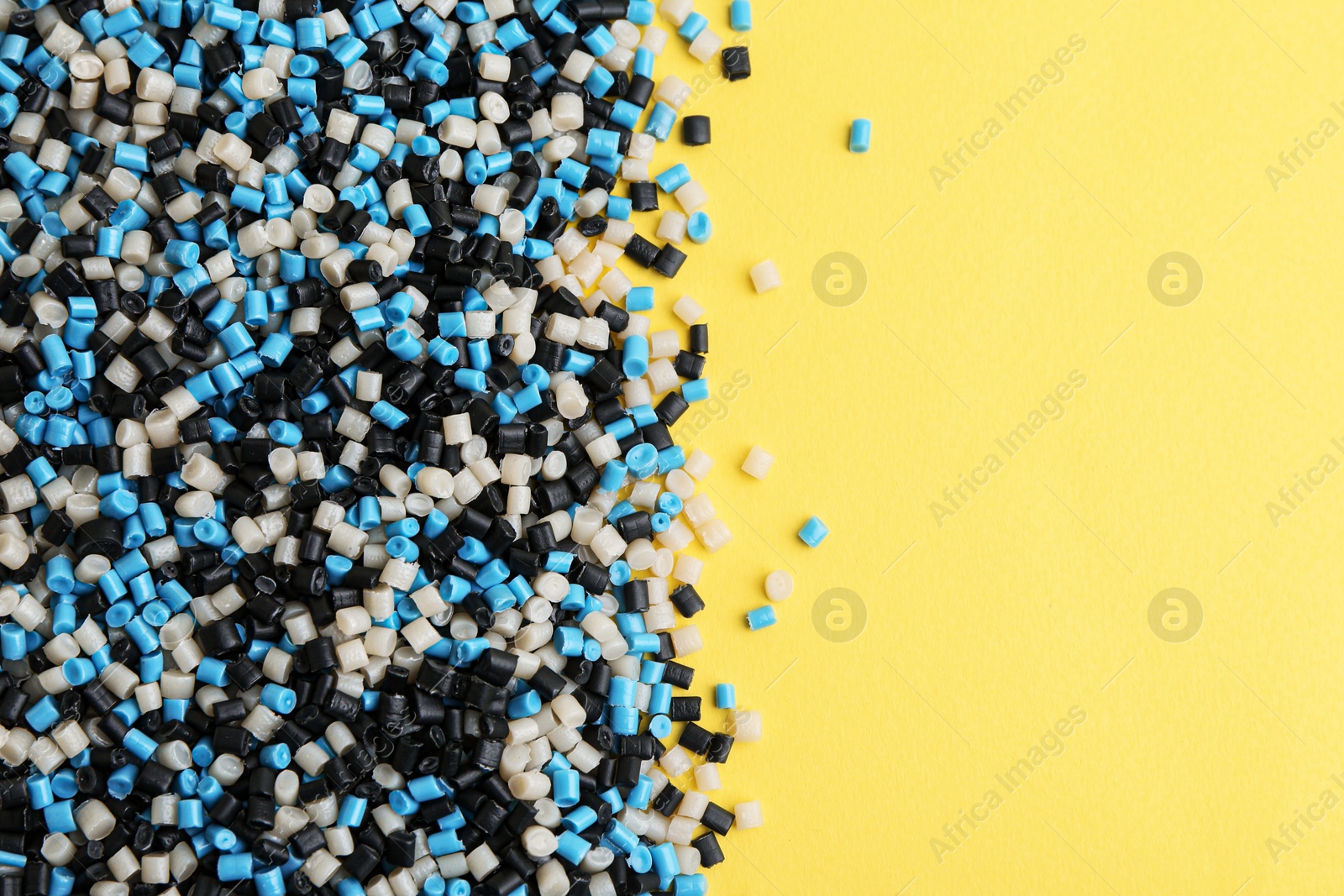 Photo of Pile of colorful plastic granules on yellow background, top view. Space for text