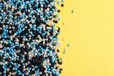 Photo of Pile of colorful plastic granules on yellow background, top view. Space for text