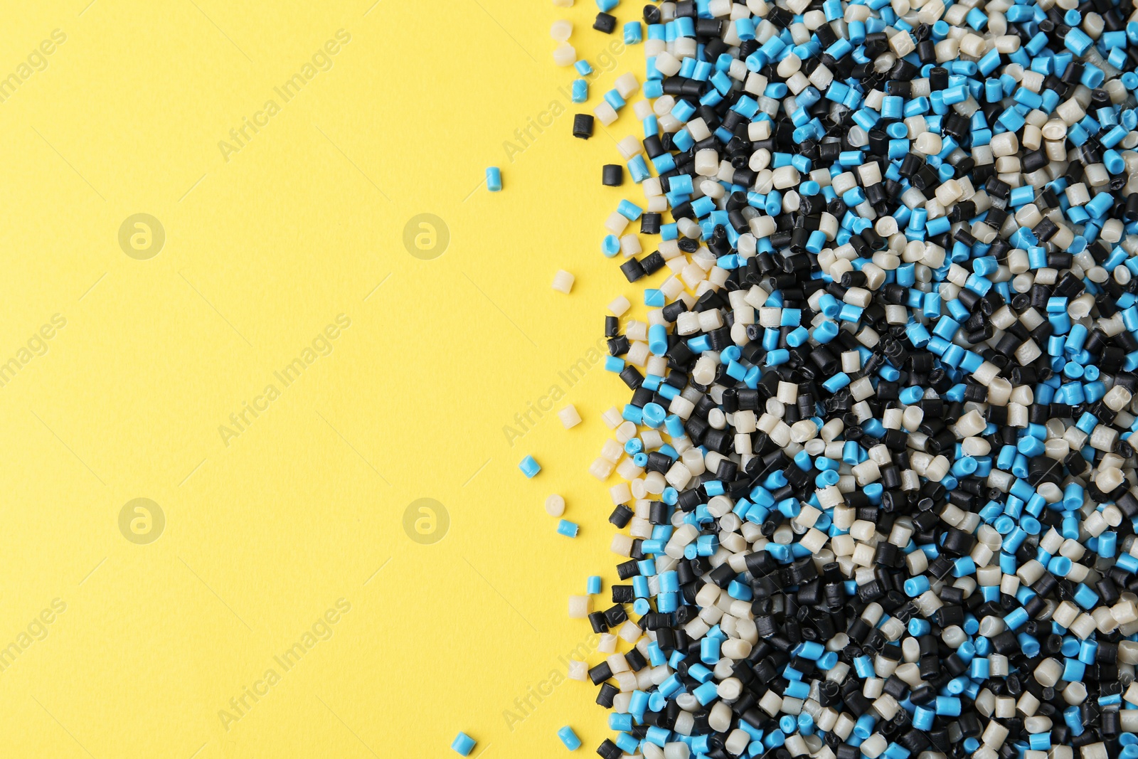 Photo of Pile of colorful plastic granules on yellow background, top view. Space for text